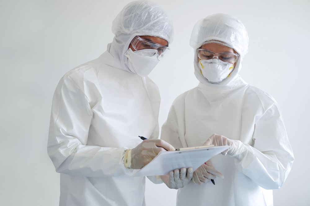 Two healthcare workers look at test results wearing N95 masks, gloves and protective outfits. Protective outfits are among the five pillars of safety for healthcare settings.