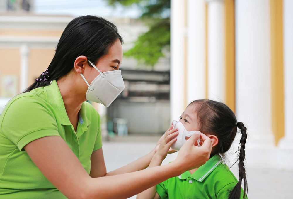 Mother helping her young daughter put an N95 mask on.