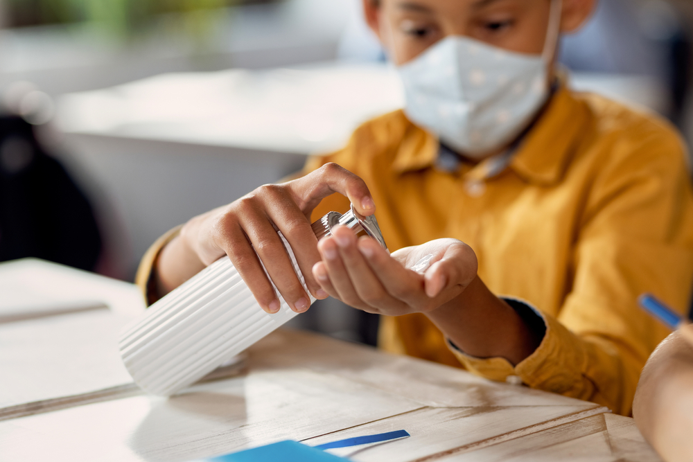 Child using hand-sanitizer in an elementary school classroom. 